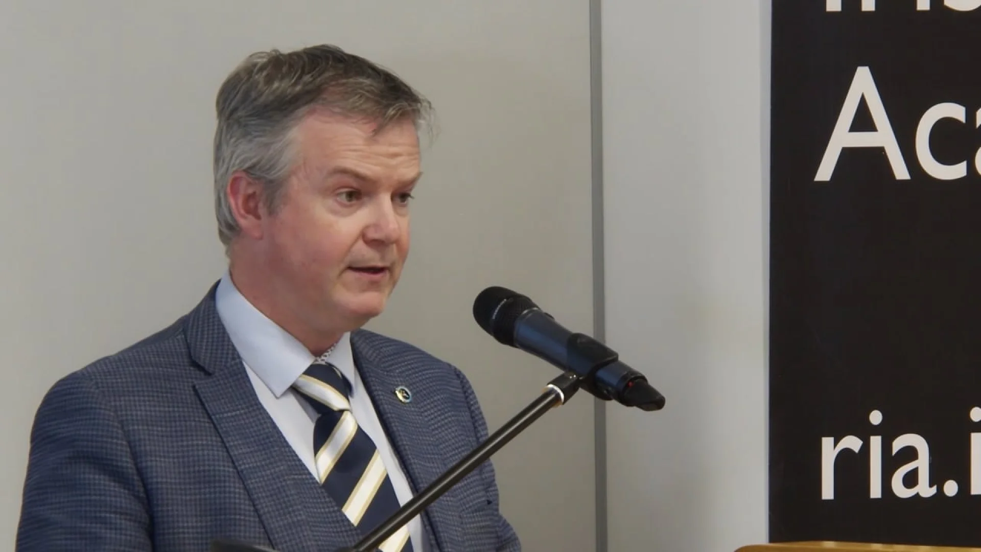 A speaker discusses brand development strategy at the Rhyming Weavers Anniversary: Part Five event, standing before a branded backdrop.
