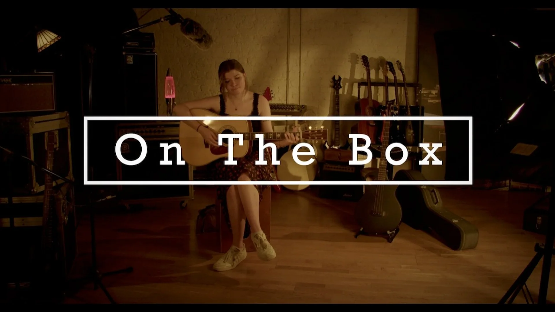 Evie Dowden performs acoustic guitar in a warm-lit studio for the On the Box series, showcasing creative brand development and musical artistry.